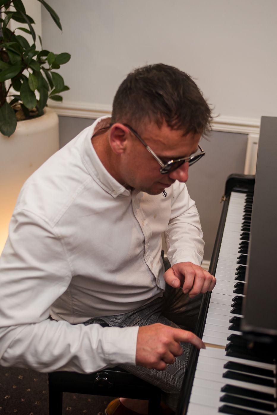 Person in white shirt playing piano in a well-lit room with indoor plants.