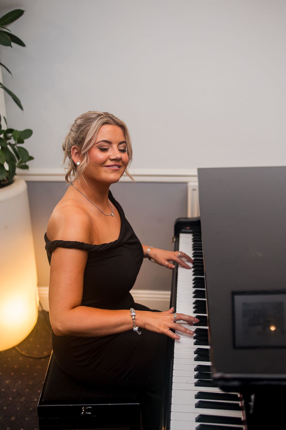 Woman in black dress playing piano with joyful expression.
