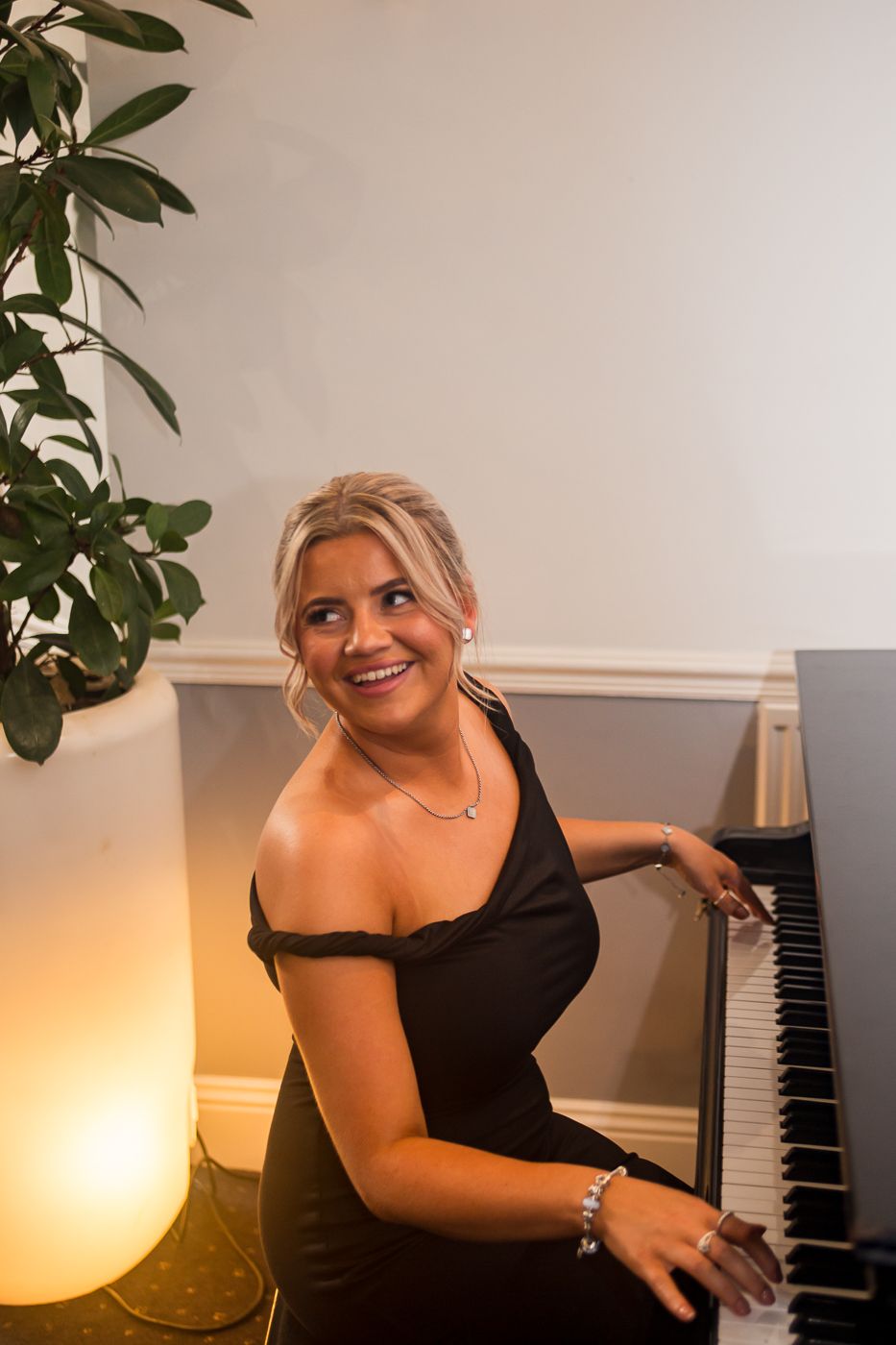 Woman in elegant black dress smiling while seated at piano.