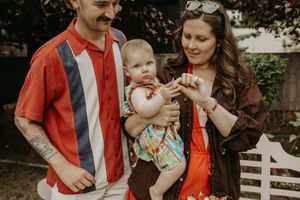 A family in coordinating red and brown outfits poses together in front of a white fence during an outdoor photo session.