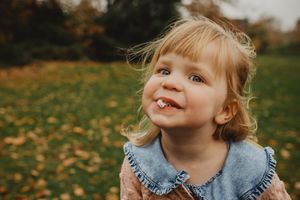 A joyful child wearing a denim dress plays in autumn leaves on a sunny fall day.