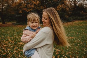 Parent and child share joyful moments together while playing in a park filled with autumn leaves.