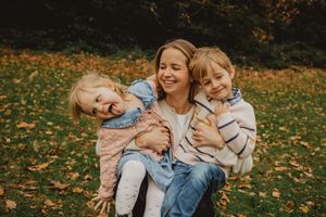 Family members share joyful moments together while playing in fallen autumn leaves on a sunny day.