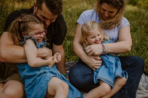 A loving family sits together on grass in matching denim outfits during an outdoor photo session.