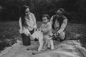 A family relaxes together on a blanket in a park during a black and white outdoor photoshoot.