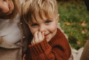 A child wearing a cozy brown knit sweater plays outdoors in autumn while making a playful expression.