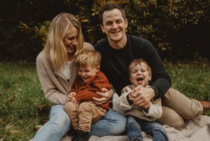 A family sits together on grass during a fall photo session in warm earth tones.