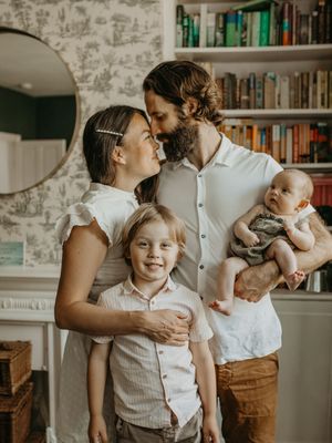 A family shares tender moments together in a cozy home library with white walls and built-in bookshelves.