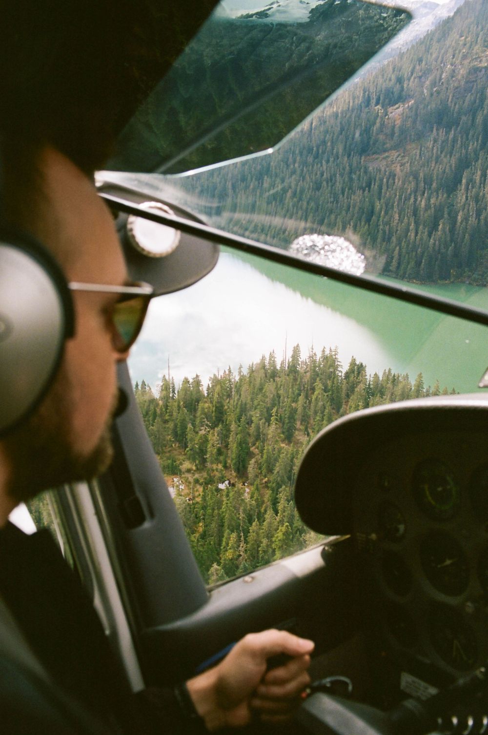 Pilot flying small aircraft over scenic mountain landscape with emerald lake below.