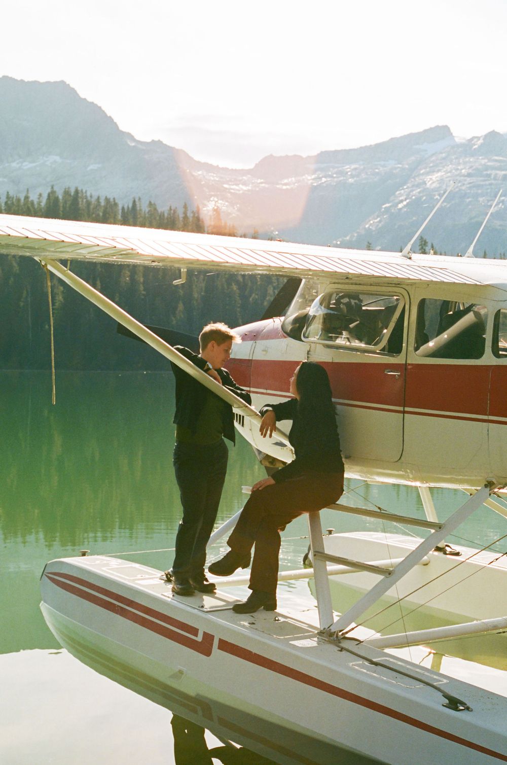 Two people boarding a seaplane on a lake with mountains in the background.