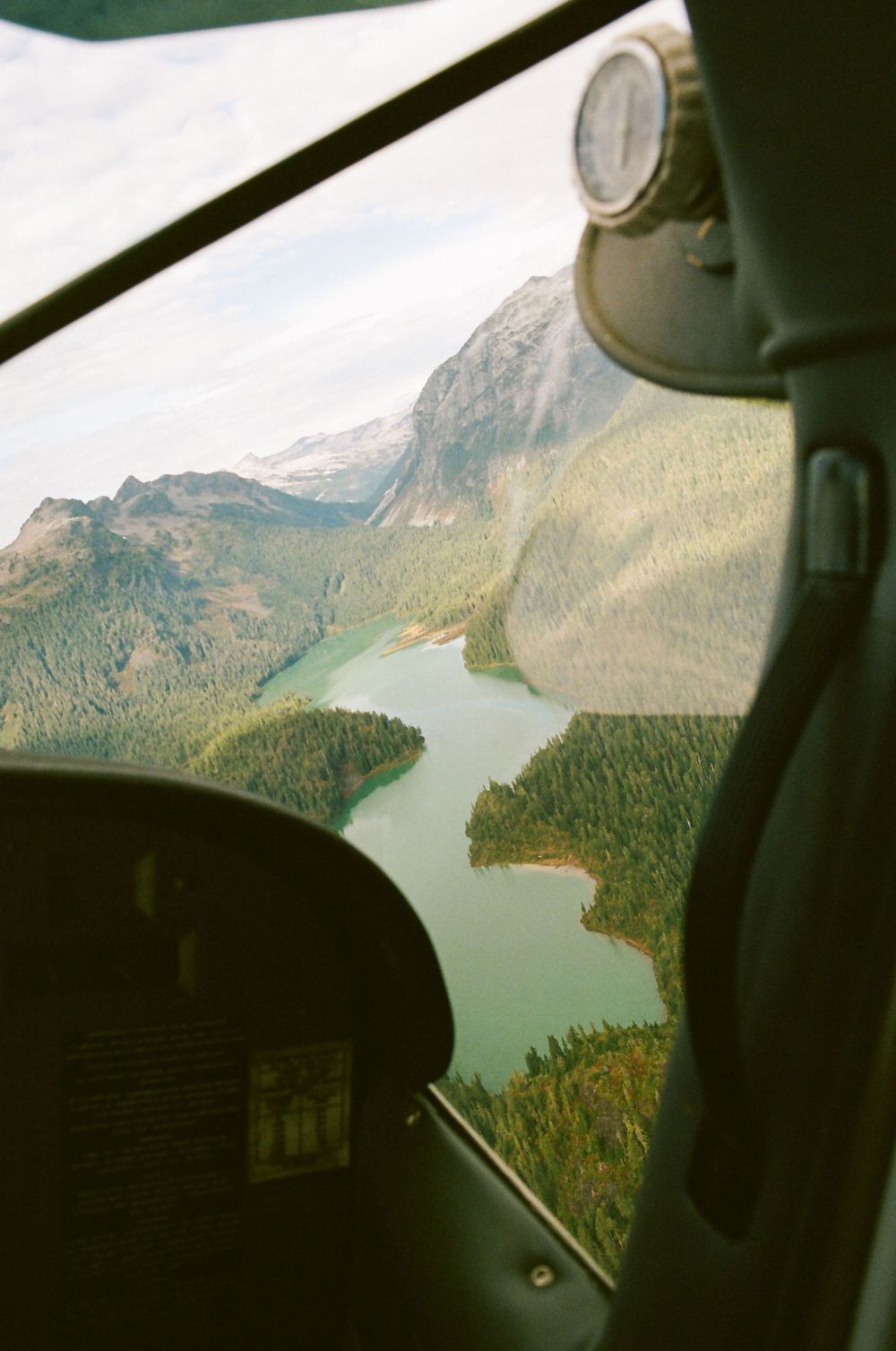 View from airplane window showing a winding turquoise lake nestled between forested mountain slopes.