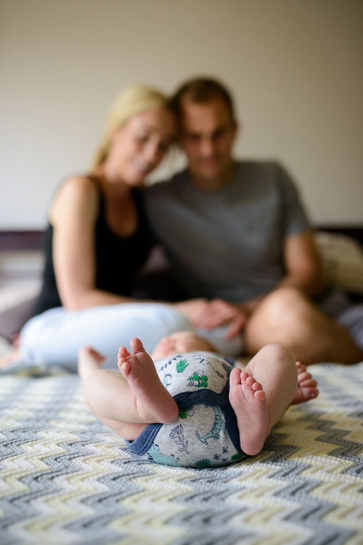 A baby lying on a bed with his mother and father blurry in the background - Kelly Chapman Photographer Perth