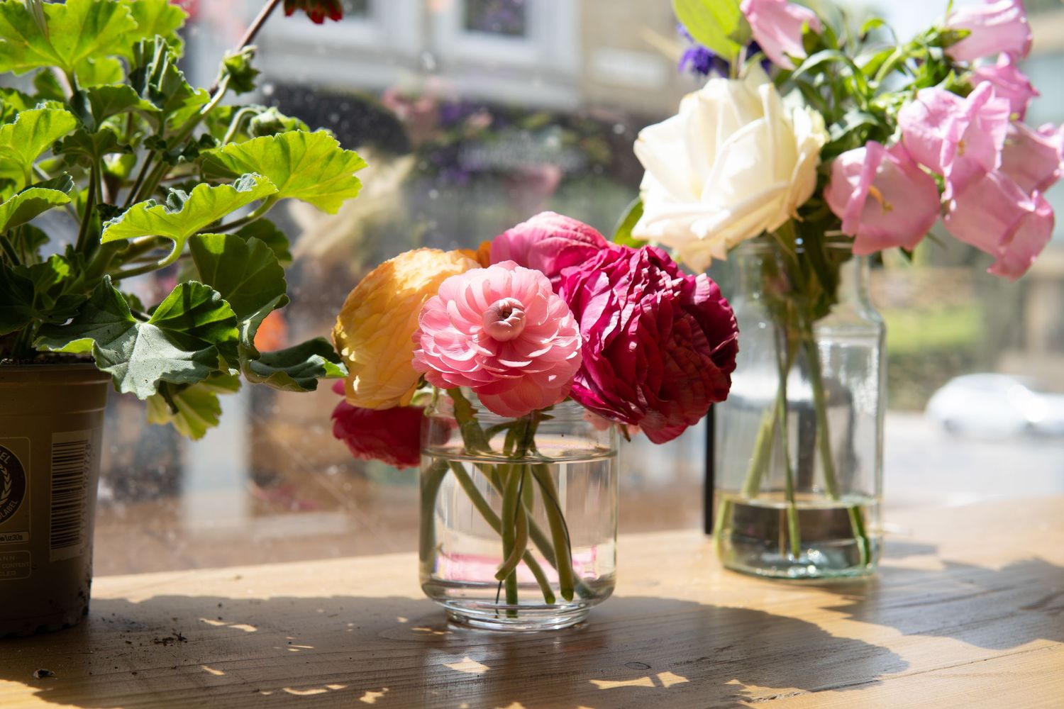 Still-life photograph of a glass jar filled with pink and white peonies, arranged on a wooden table and photographed in natural window light