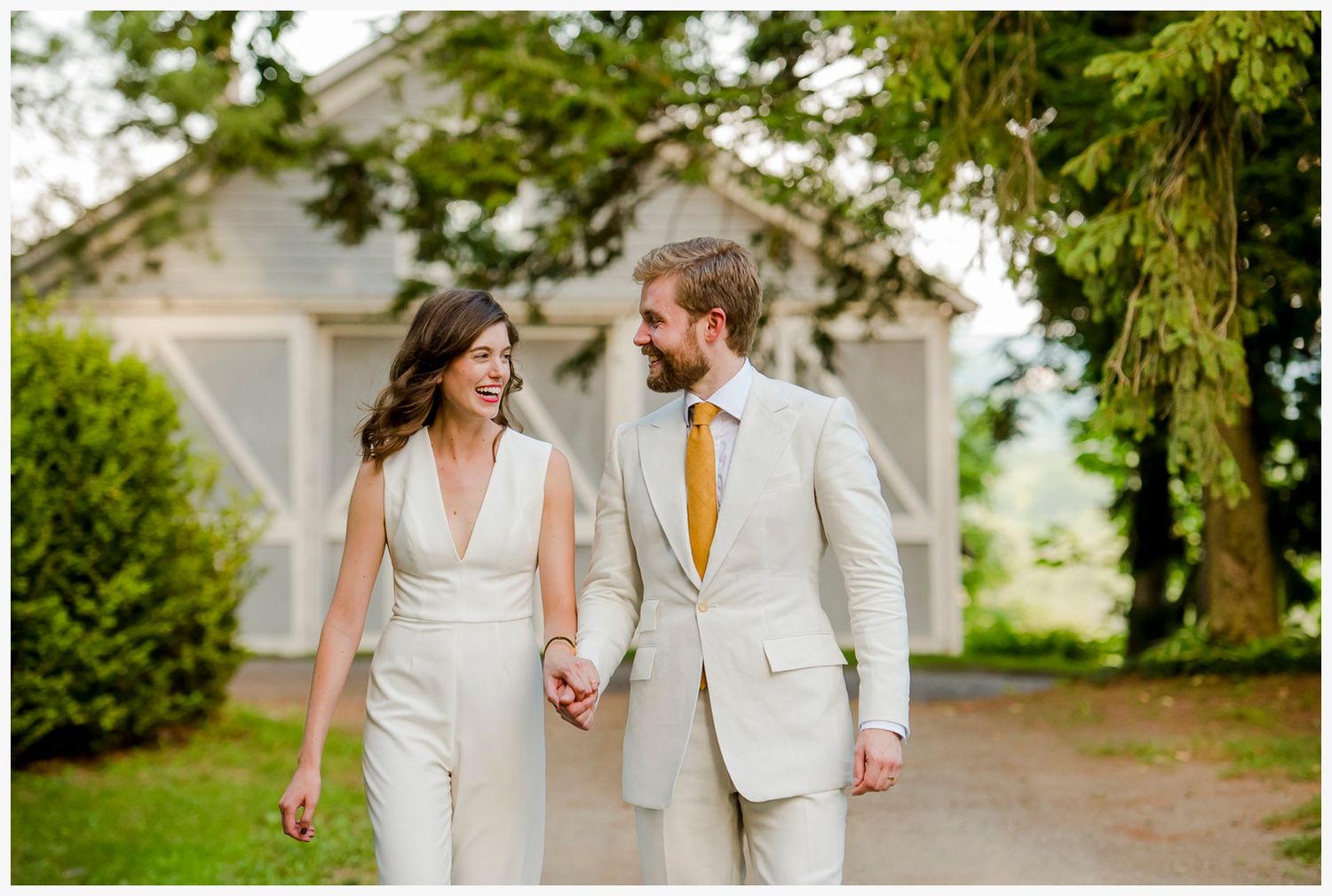 Modern couple in matching light colored suits walking together on garden path.