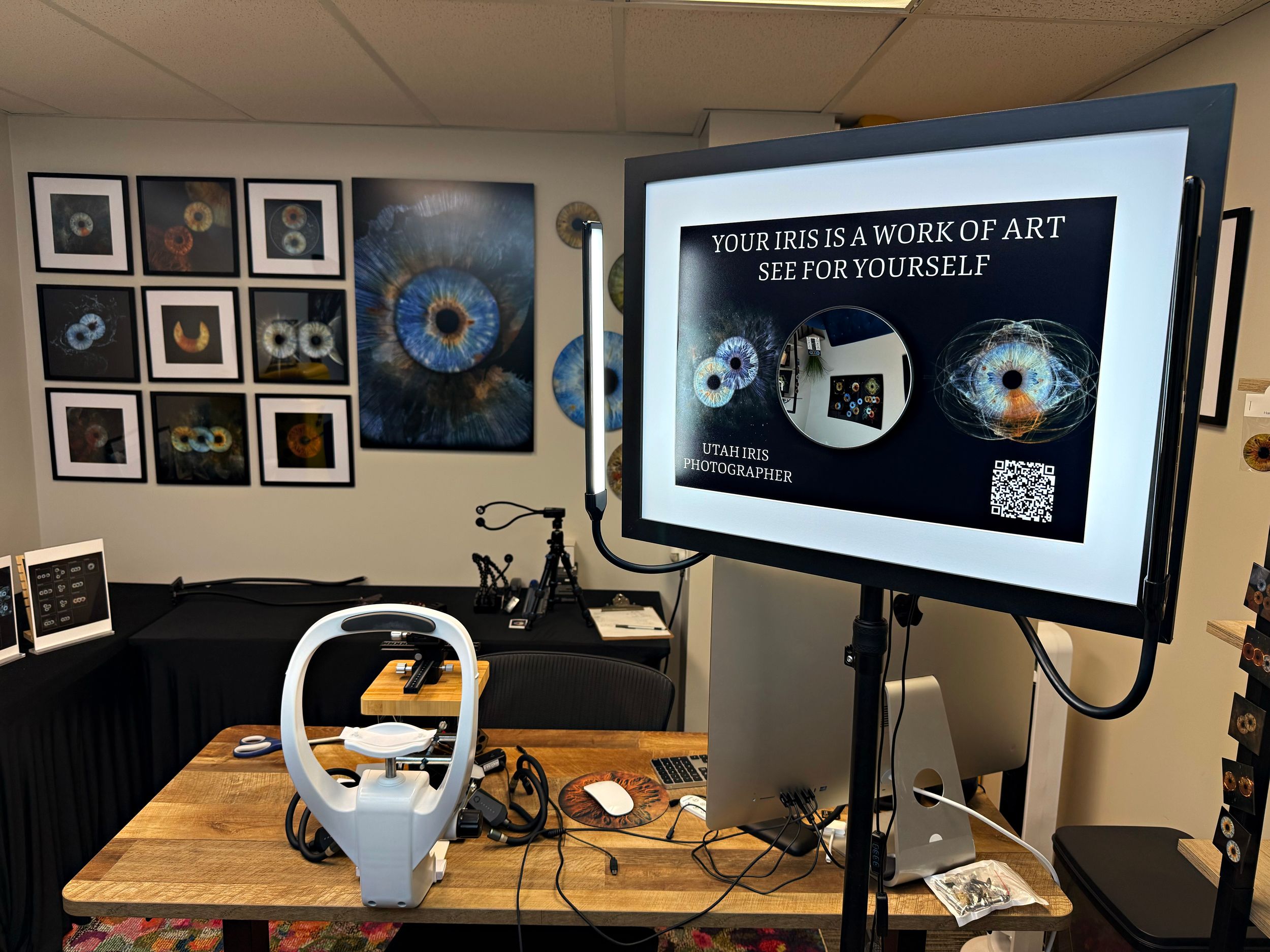 A monitor displays digital art content next to framed artwork on a wall, with a teapot sitting on a wooden desk.