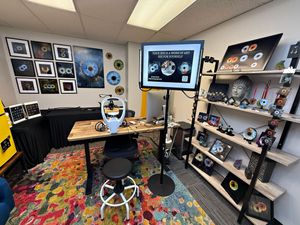 A panoramic view of a creative workspace with shelves displaying collectibles, photos, and gaming memorabilia.