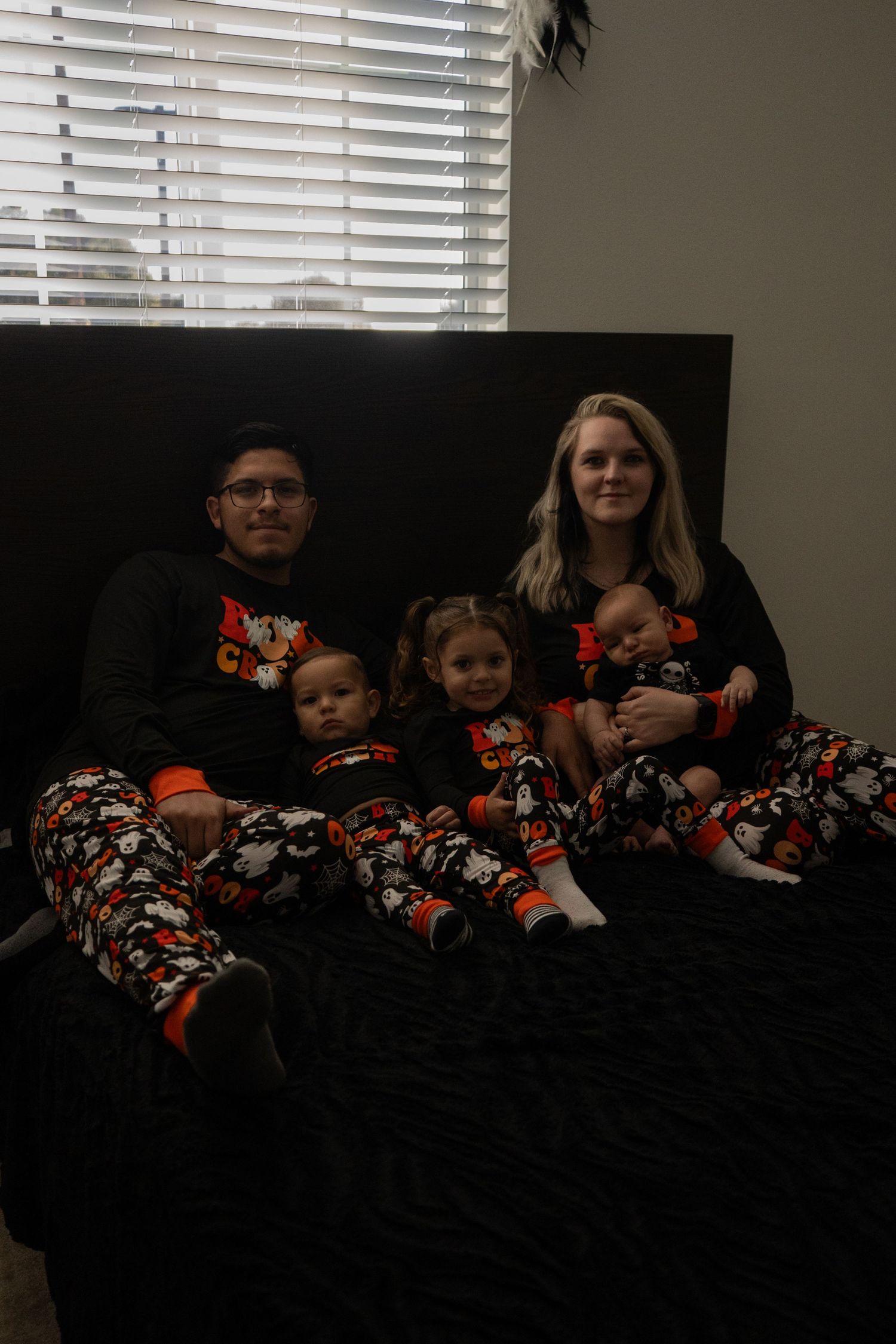 A family wearing matching black and orange floral pajamas sits together on a dark couch.