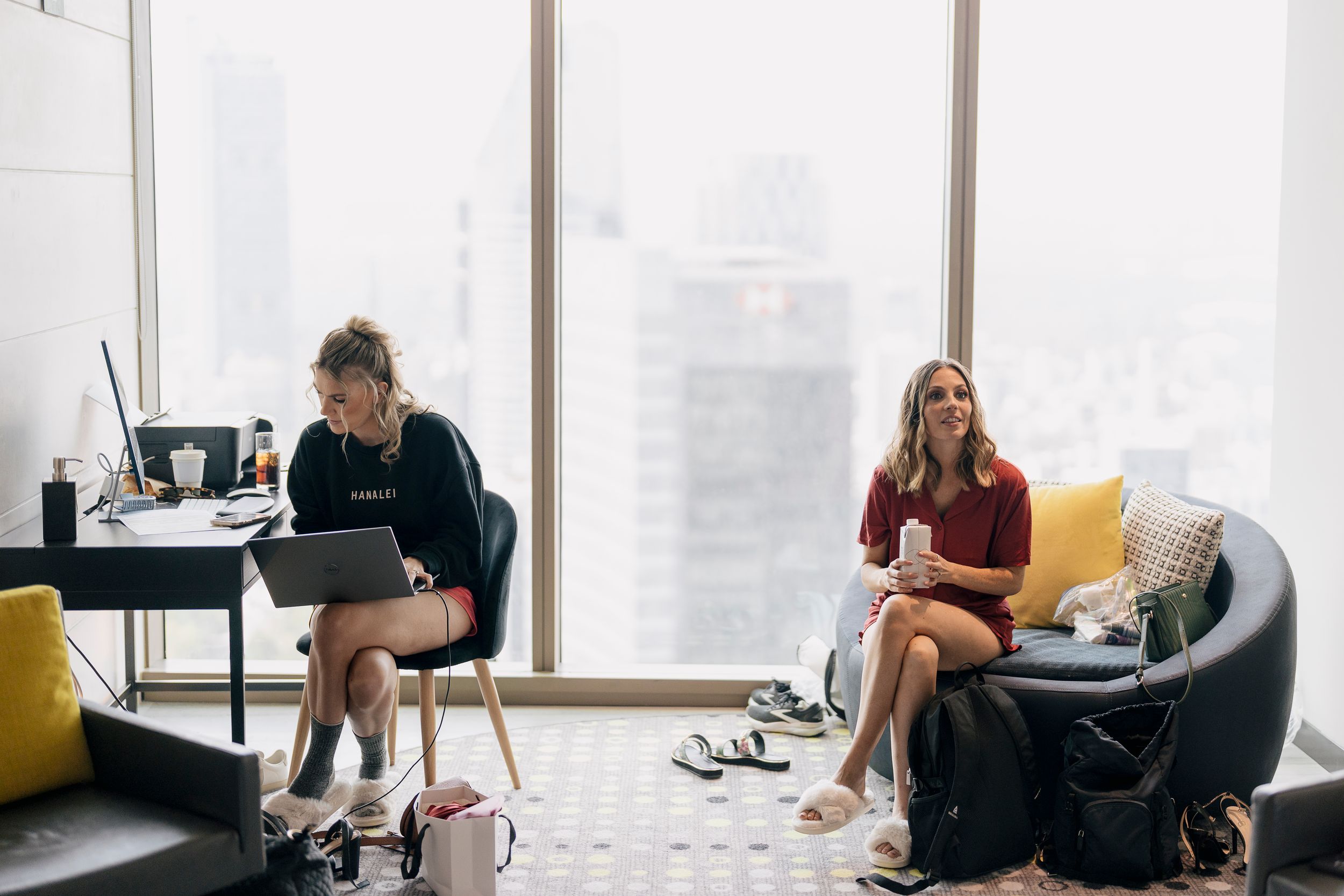 Two people working on laptops in a modern office space with large windows and city views in the background.