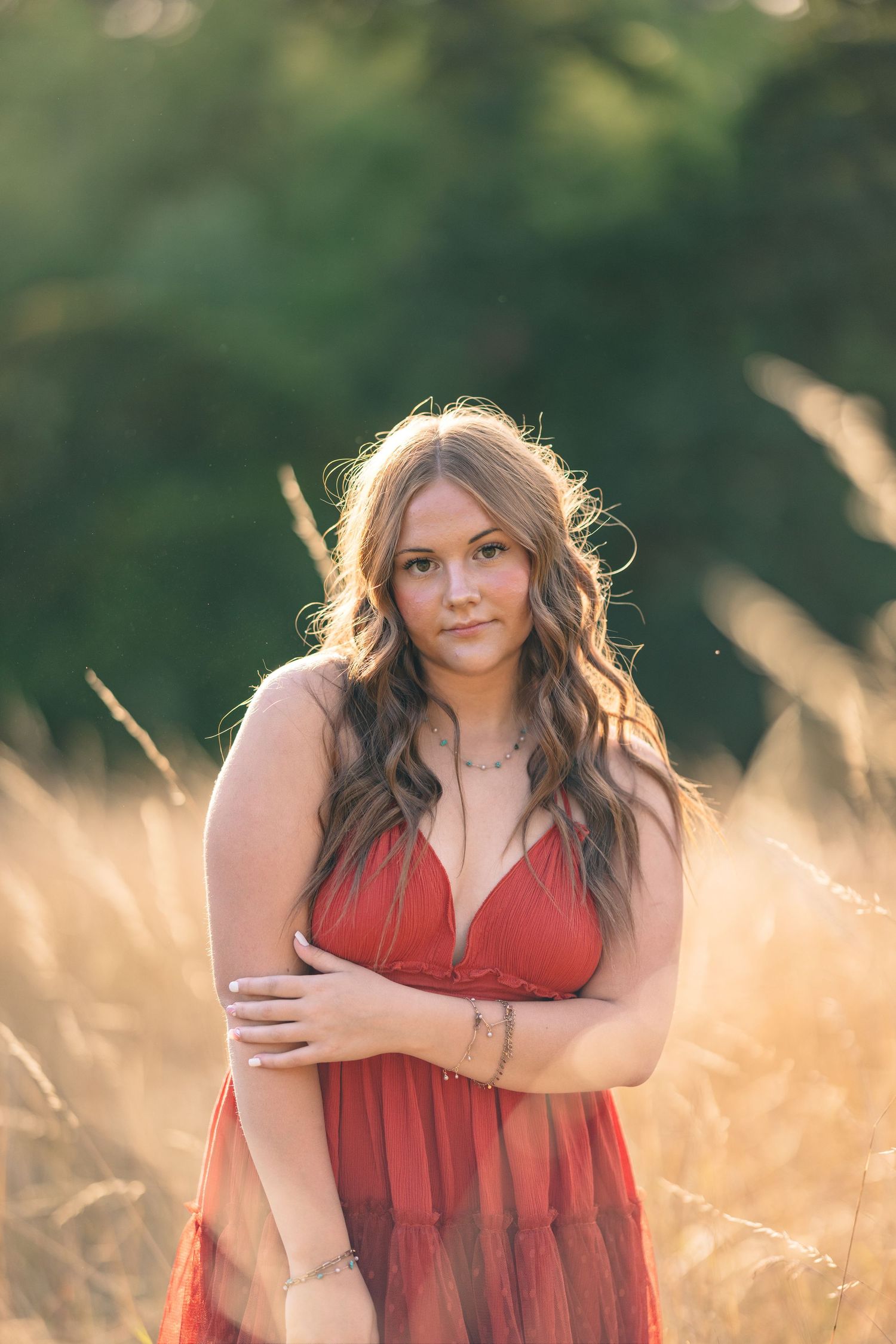 Woman in red dress poses gracefully in sun-kissed field of tall grass.