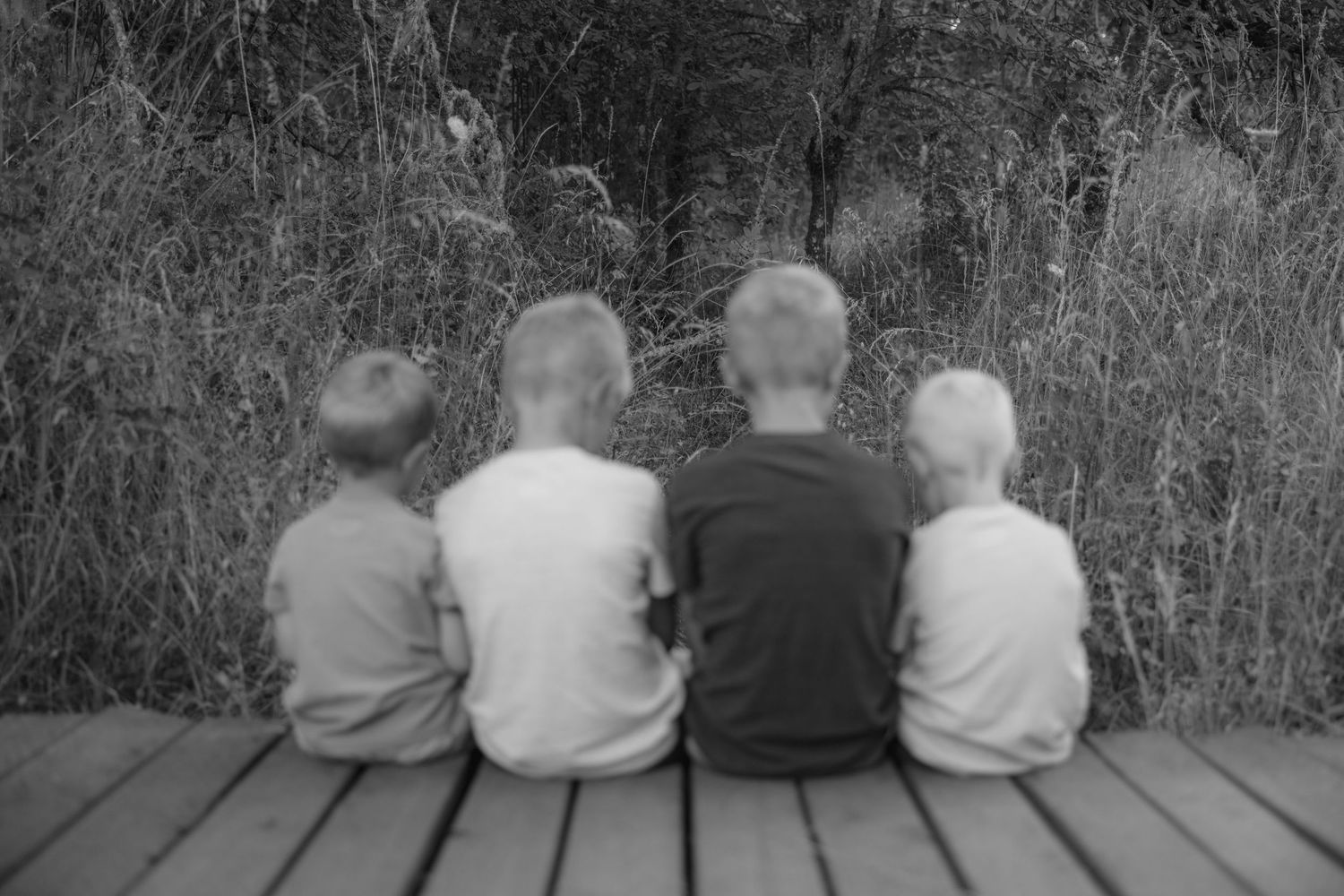 Black and white photo of children sitting together on wooden deck.