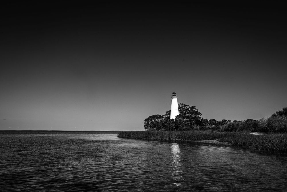 A dramatic black and white lighthouse stands tall against a dark sky on a sandy coastline.