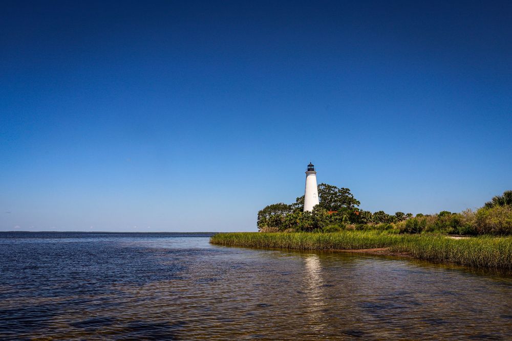 Scenic coastal lighthouse stands tall against vibrant blue sky on a sunny day at the water's edge.