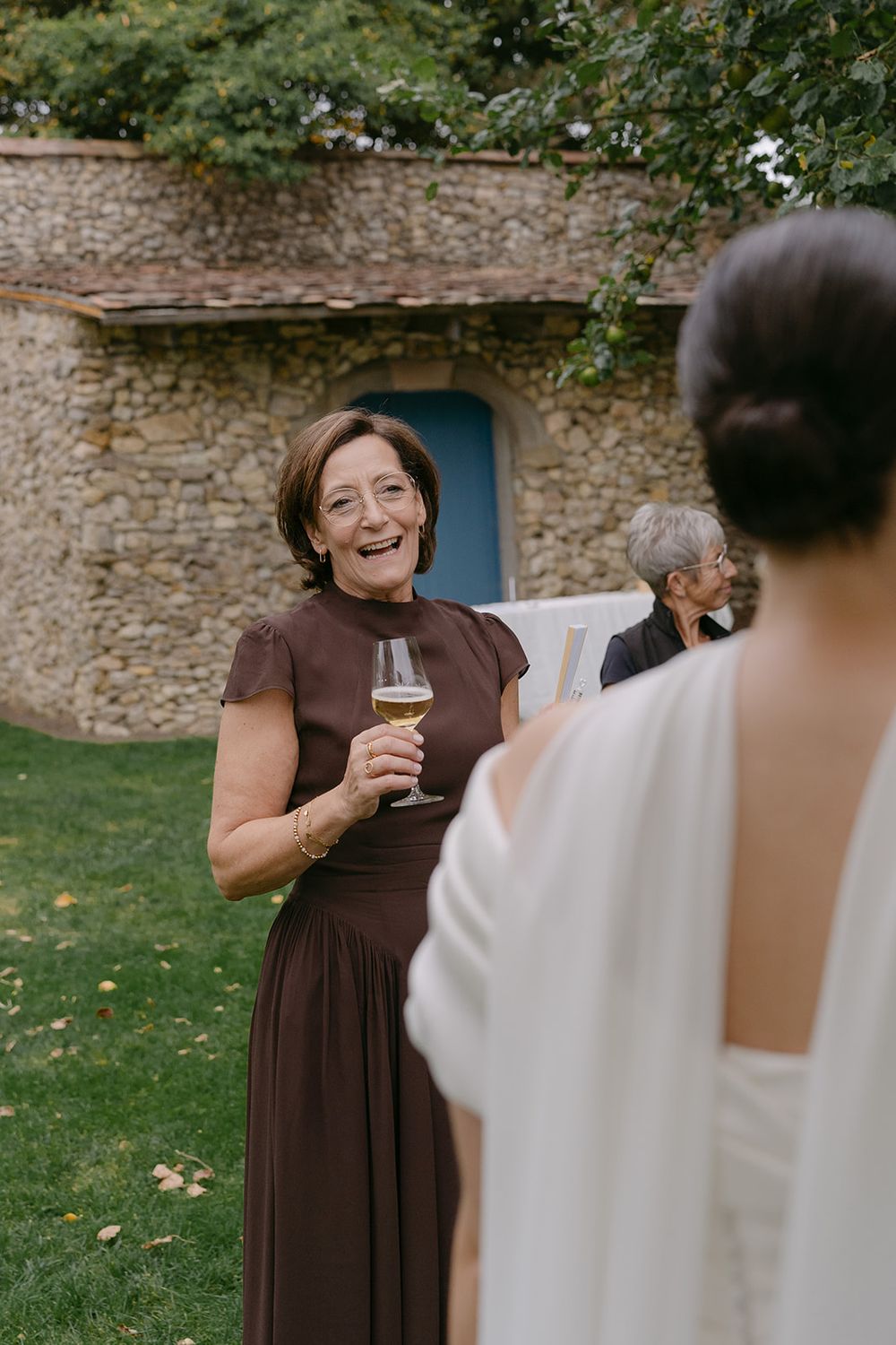 A guest in brown dress enjoying wine at an outdoor wedding reception.