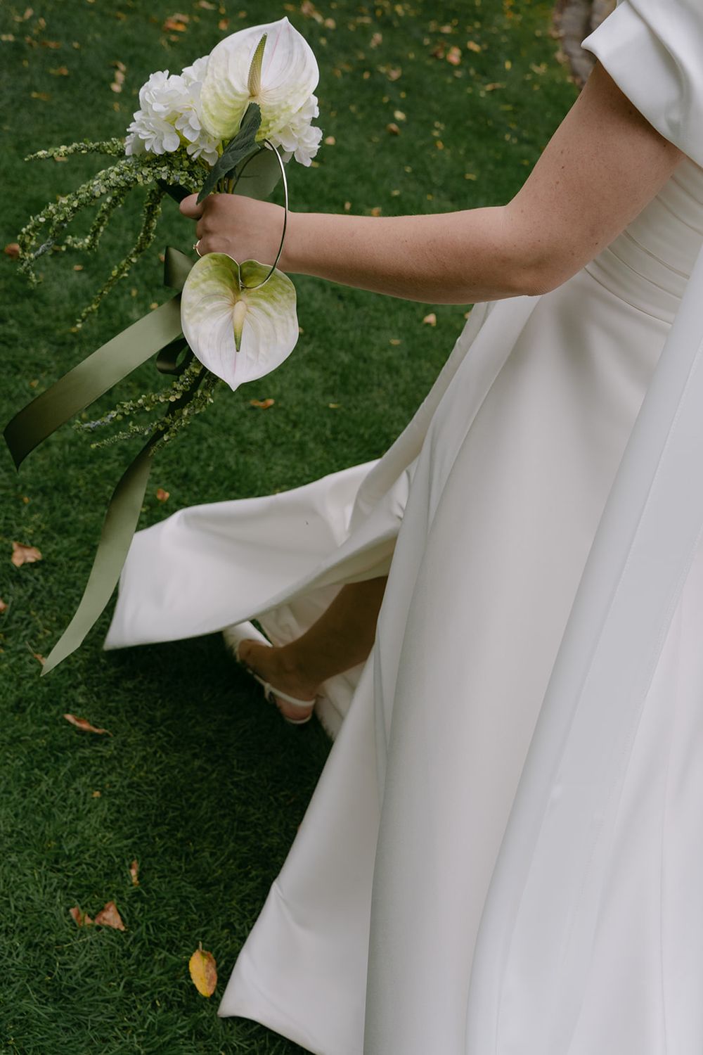 A white wedding dress and bouquet of calla lilies shown against green grass.