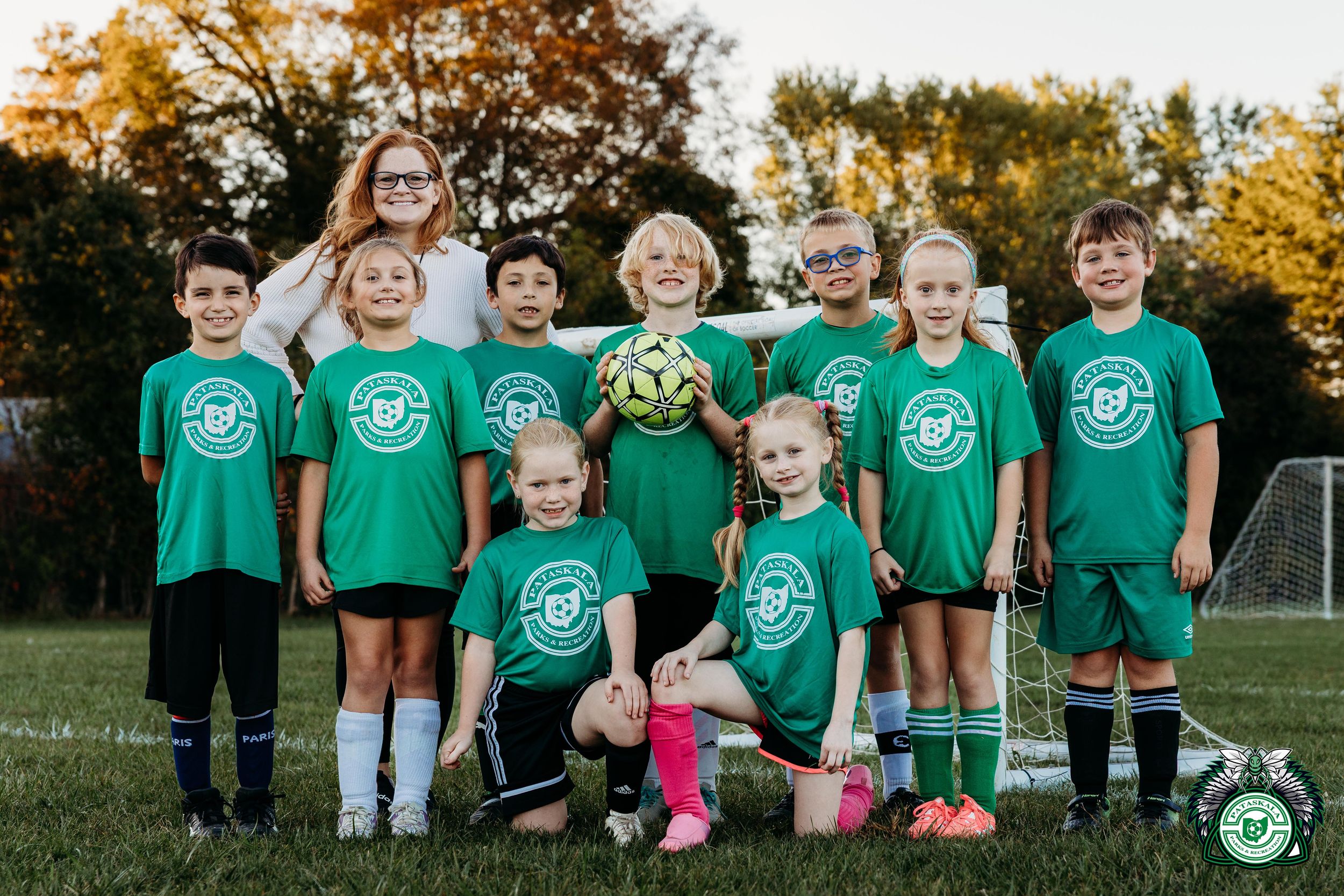 A group of children wearing matching green t-shirts pose together in a park during golden hour.