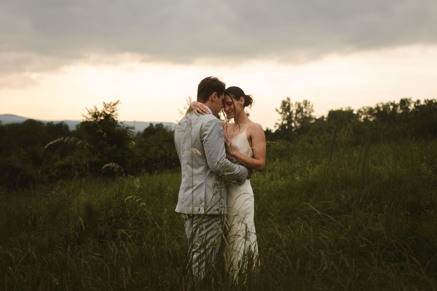 Bride and groom embrace on a hillside at sunset with panoramic mountain views at The Ruins at Sassafras in New Lebanon, NY, Hudson Valley.
