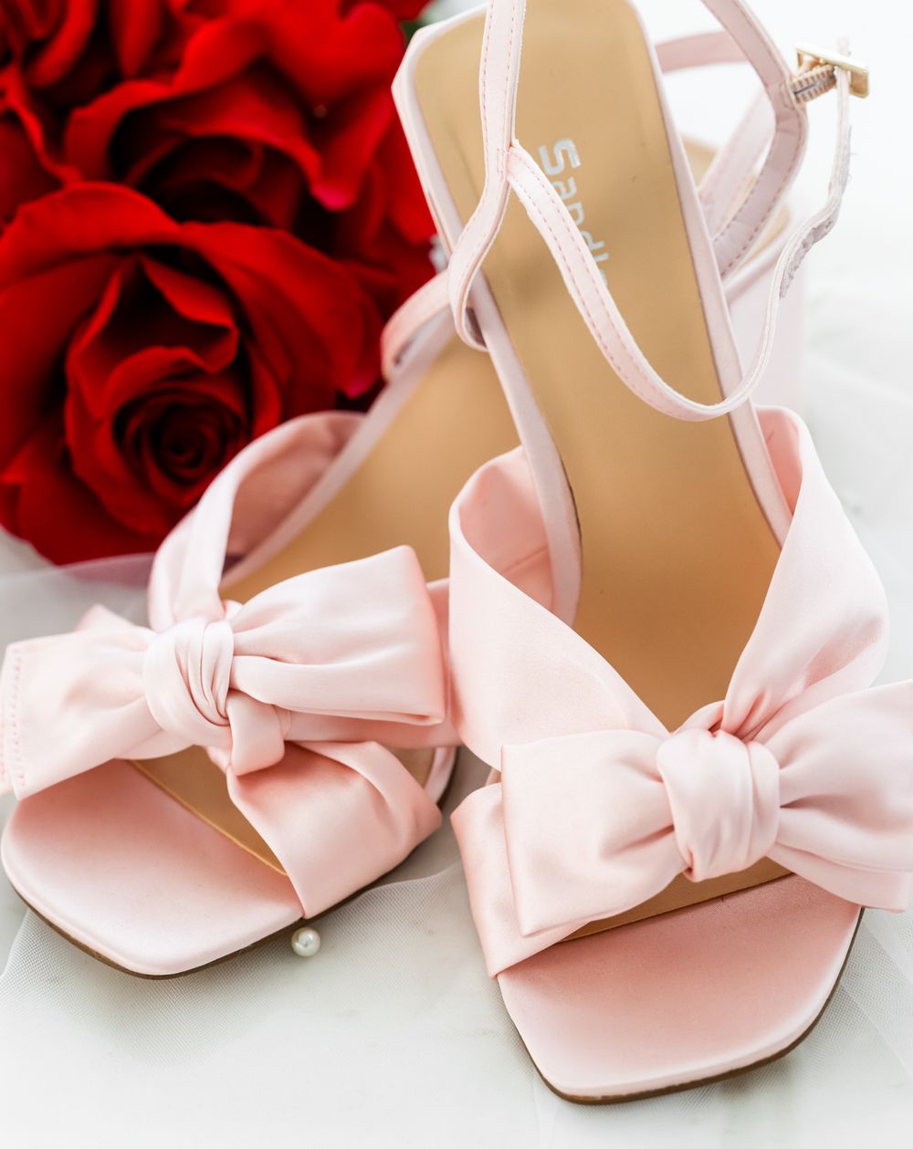Pale pink bridal shoes with large bow details displayed against red roses.