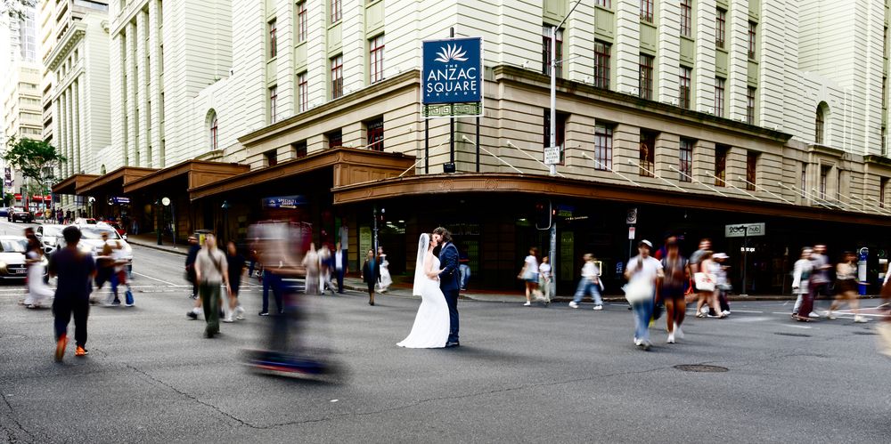 Pedestrians walk past shops and buildings on a busy urban street with motion blur effects.