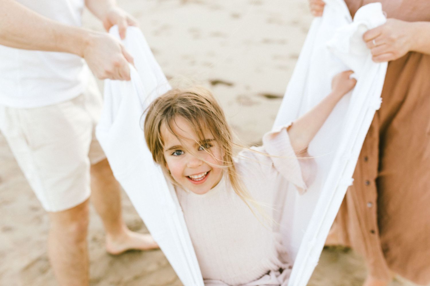 A person wearing a white sweater smiles while being wrapped in a white sheet on a beach.