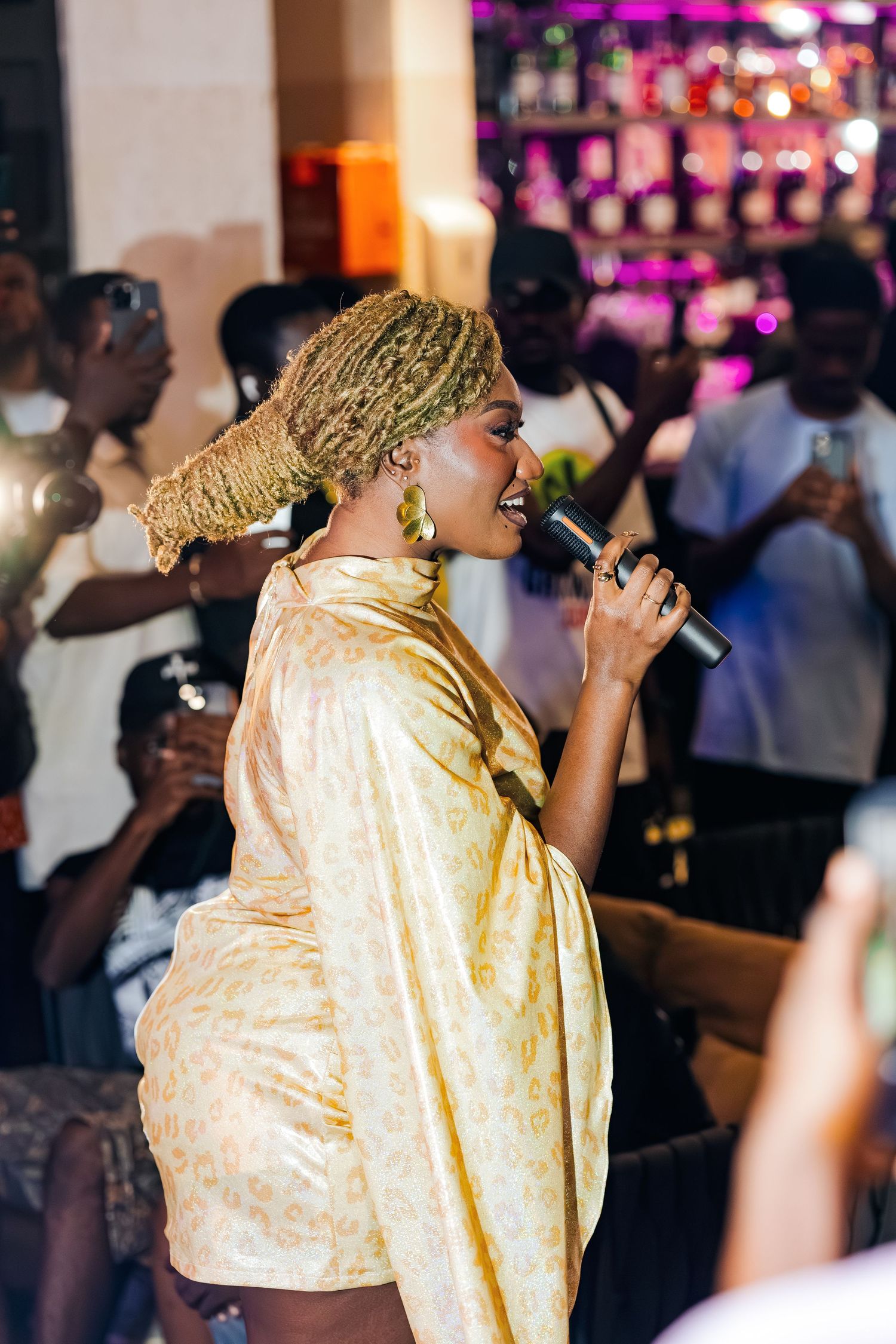 Concert performance in gold attire with colorful stage lighting and audience silhouettes.