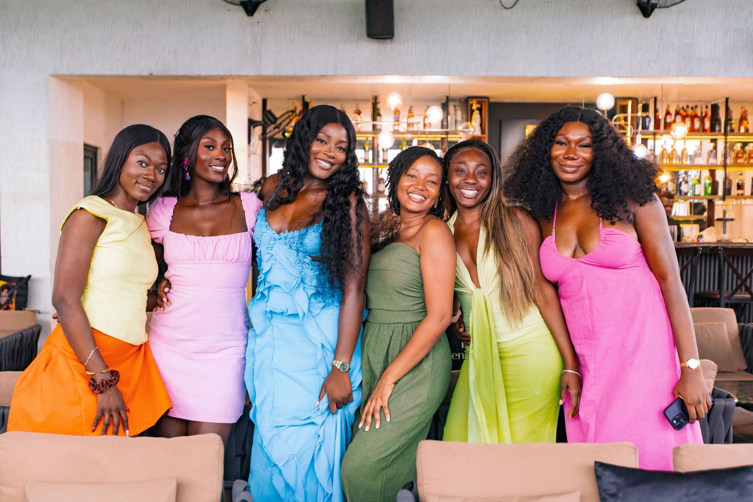 Group photo of friends wearing vibrant pastel-colored dresses at a social gathering.