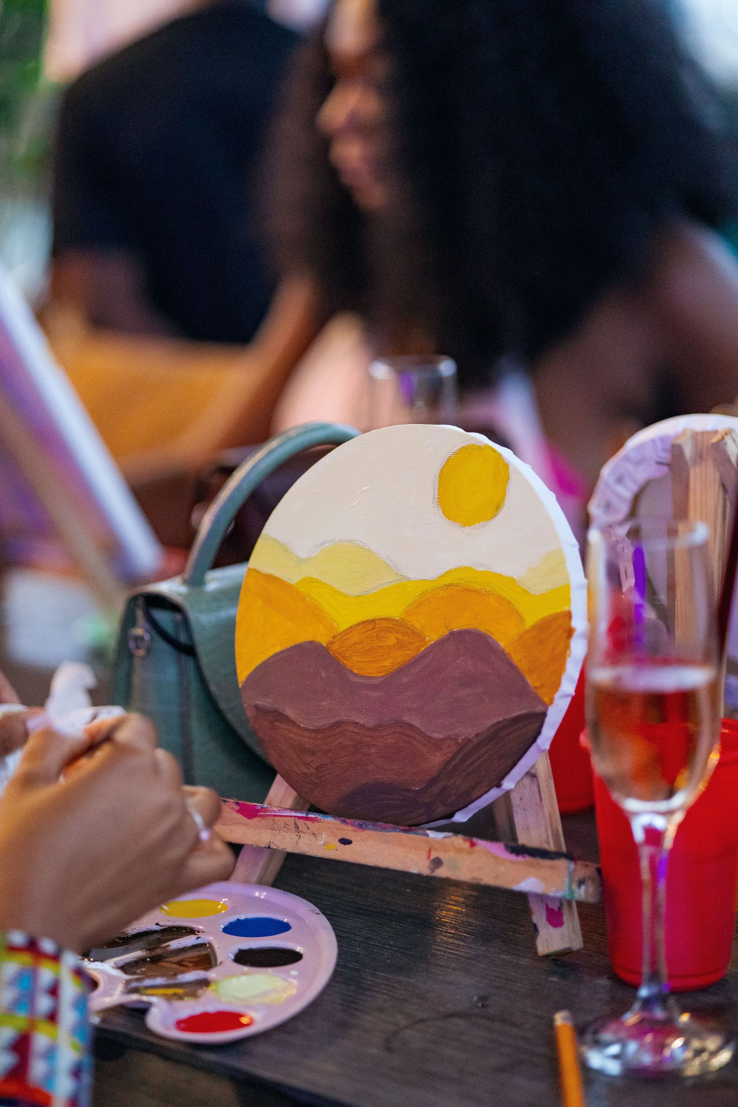 A desert landscape painting in progress with yellow sun and brown mountains on an easel.