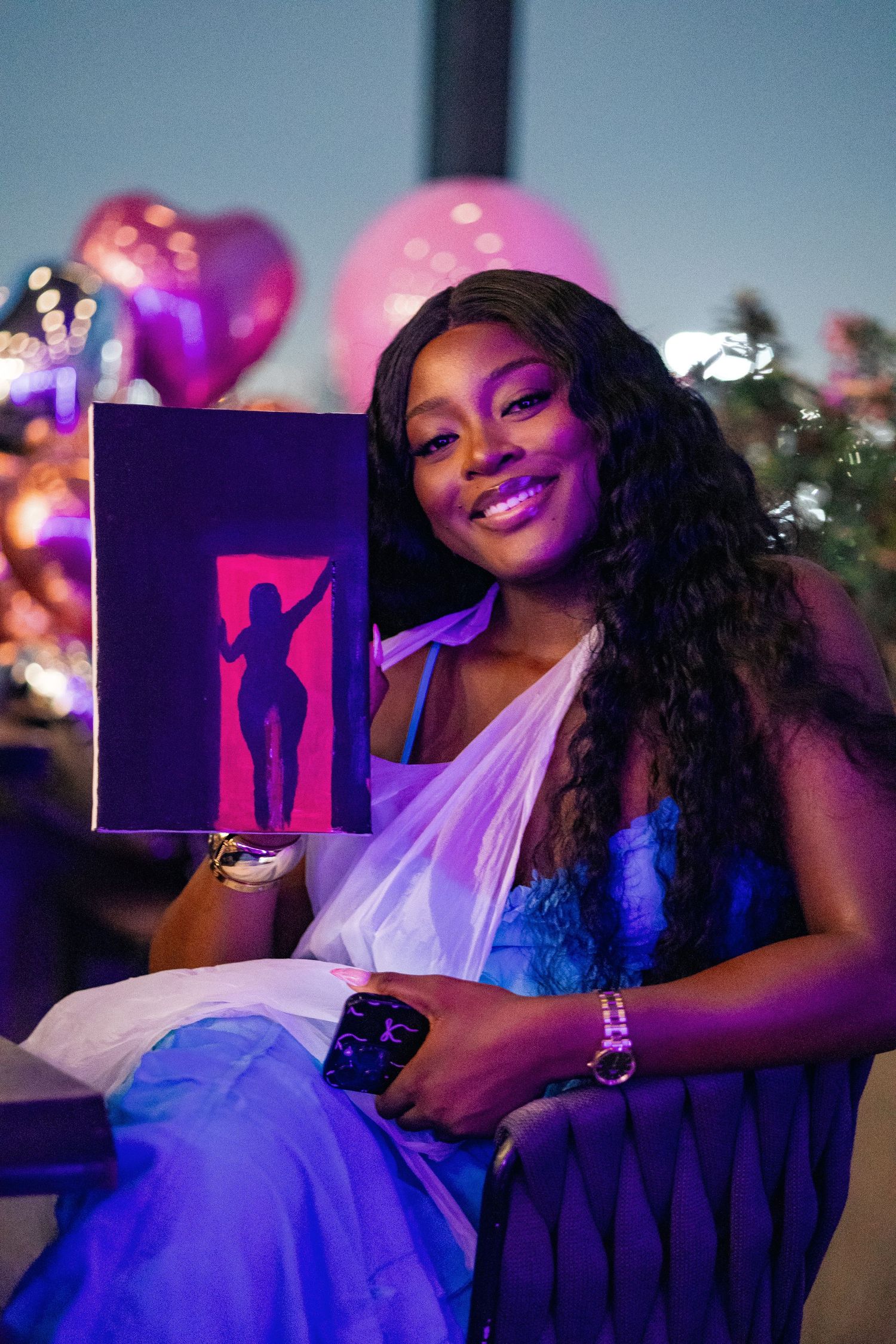 A person in evening wear holding up artwork at a nighttime event with colorful lights.