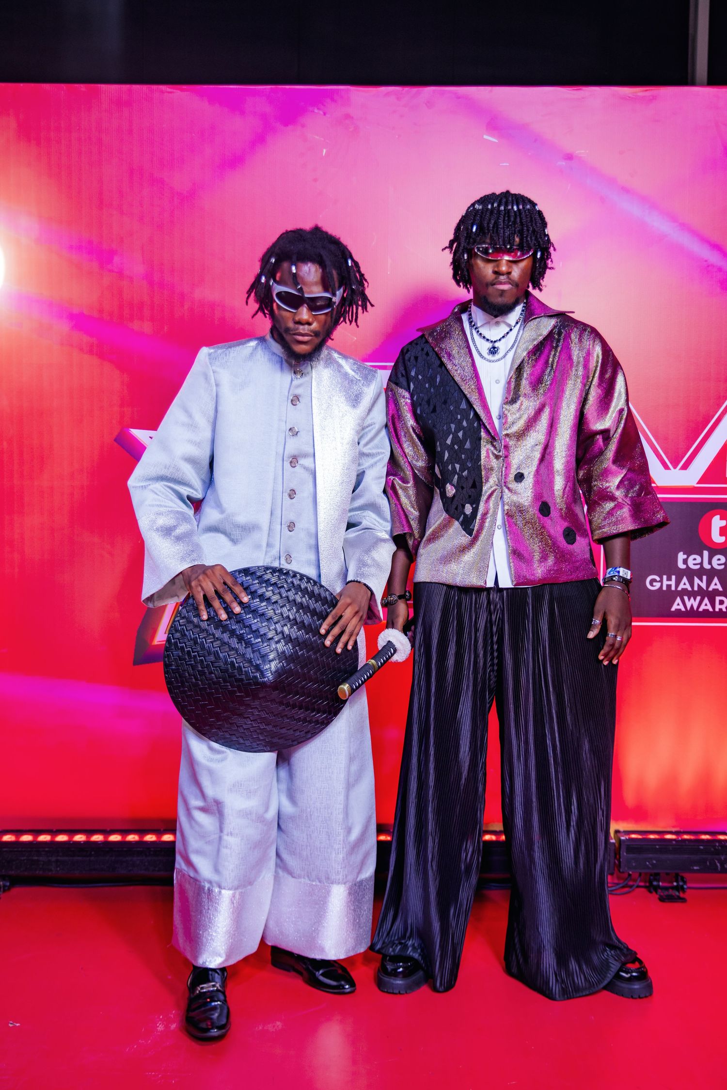 Two male artists in stylish outfits pose on red carpet at Telecel Ghana Music Awards.