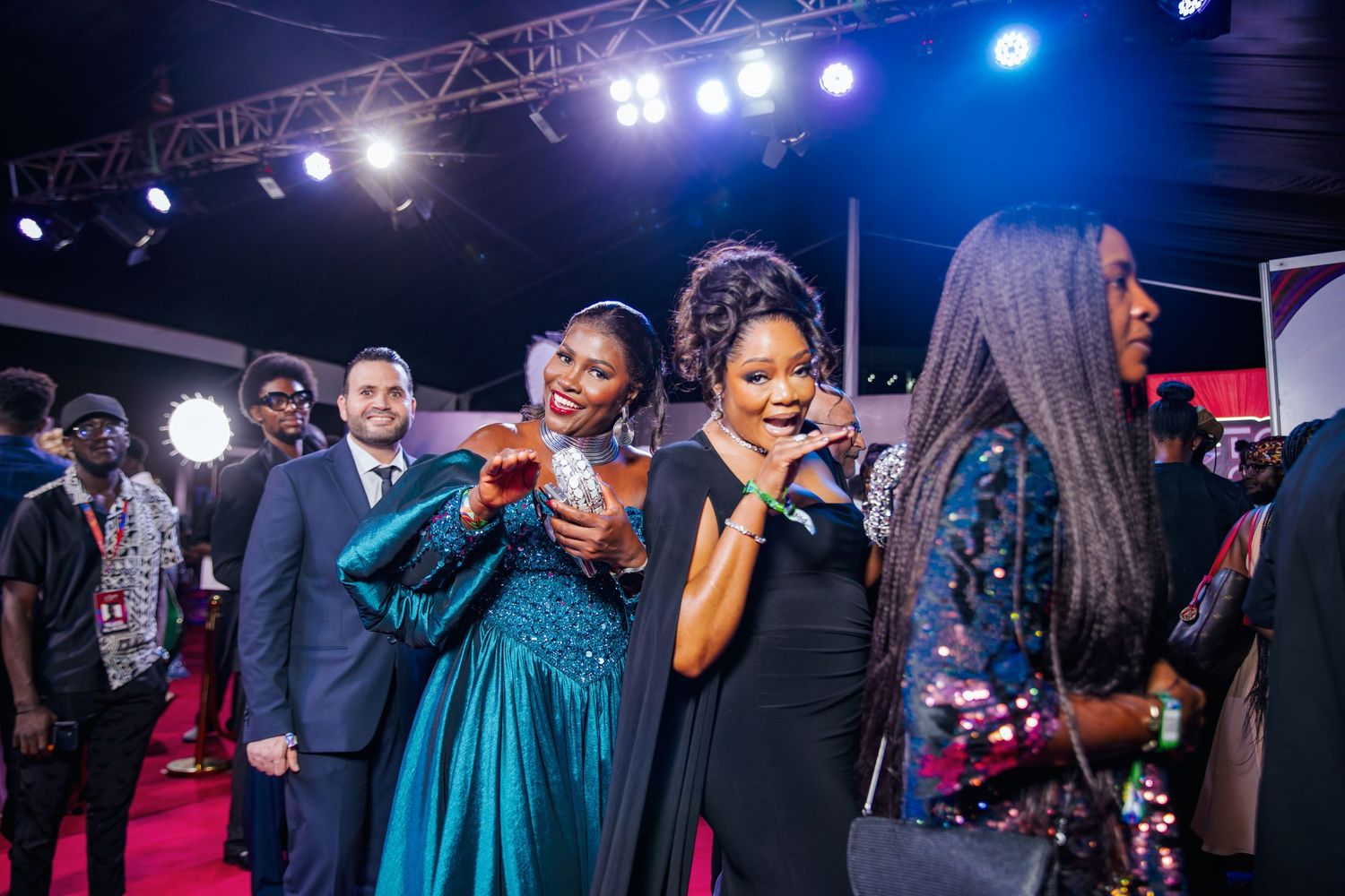 Women in elegant gowns celebrate with microphone and trophy at Ghana Music Awards event.