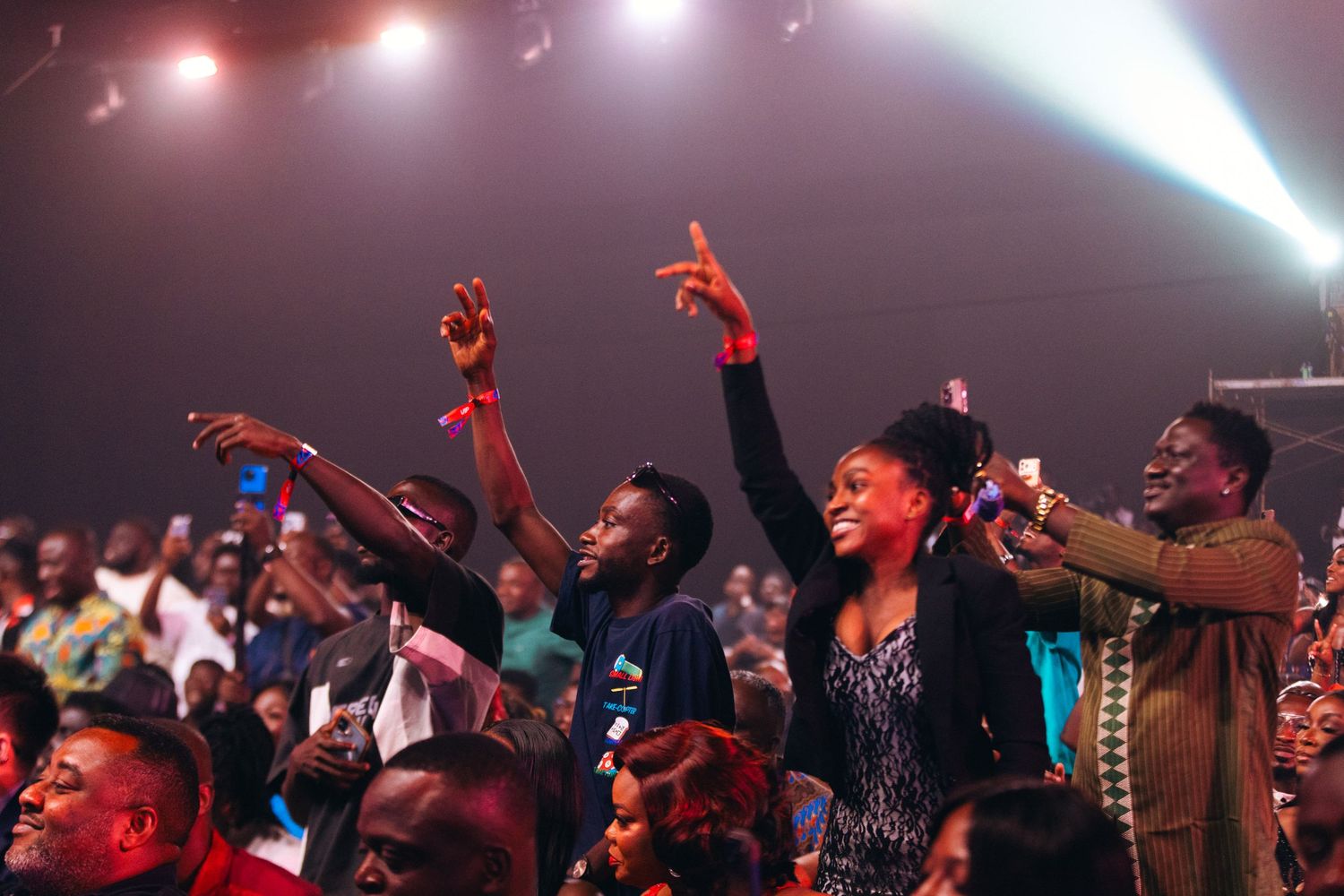 Excited crowd of people cheering and raising hands at a vibrant live concert event.