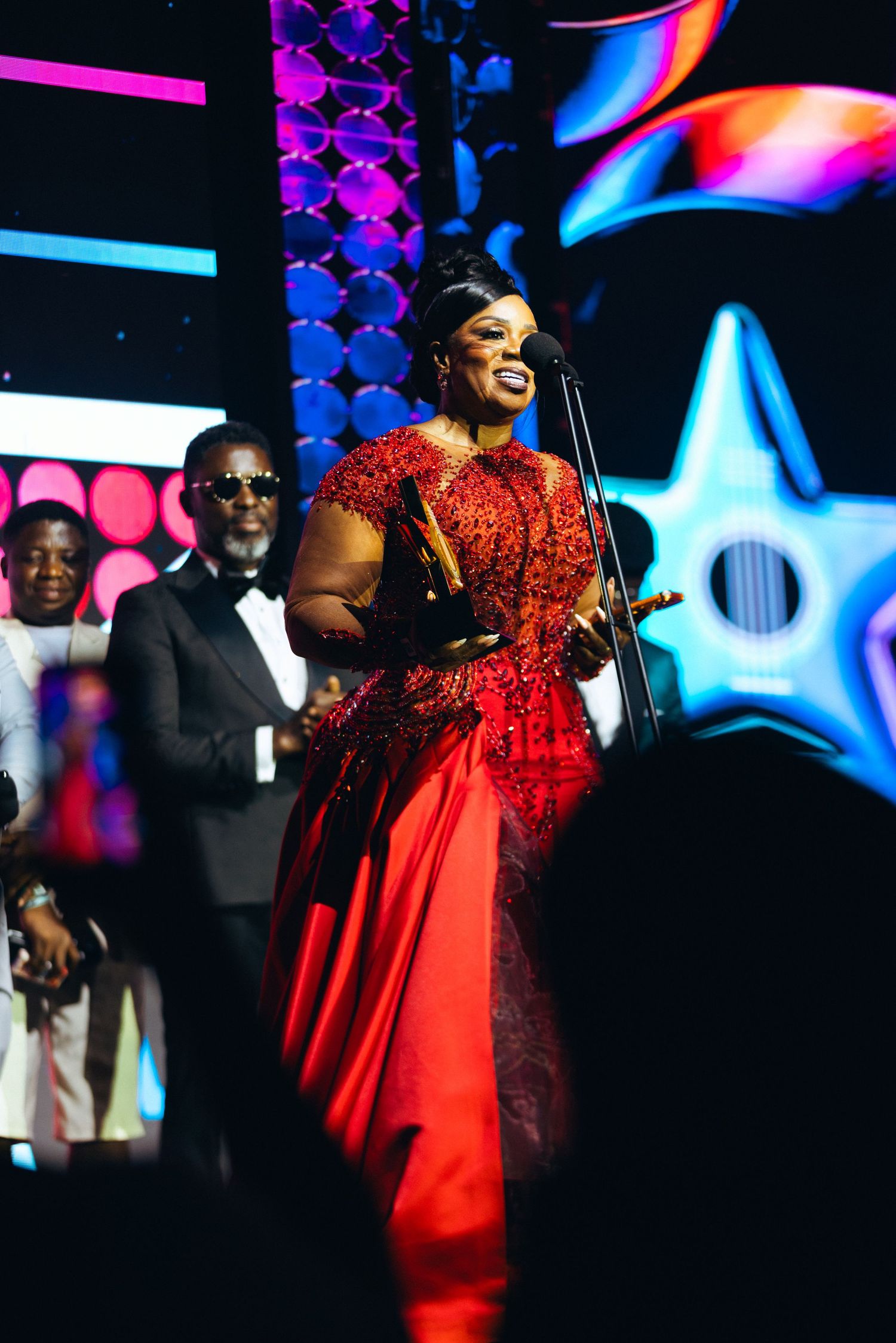 Woman in red lace gown accepts award on stage at Ghana Music Awards ceremony.
