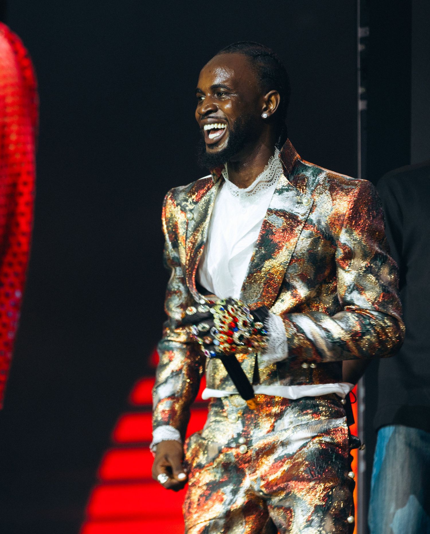 Man in gold patterned suit smiling on stage at awards show.