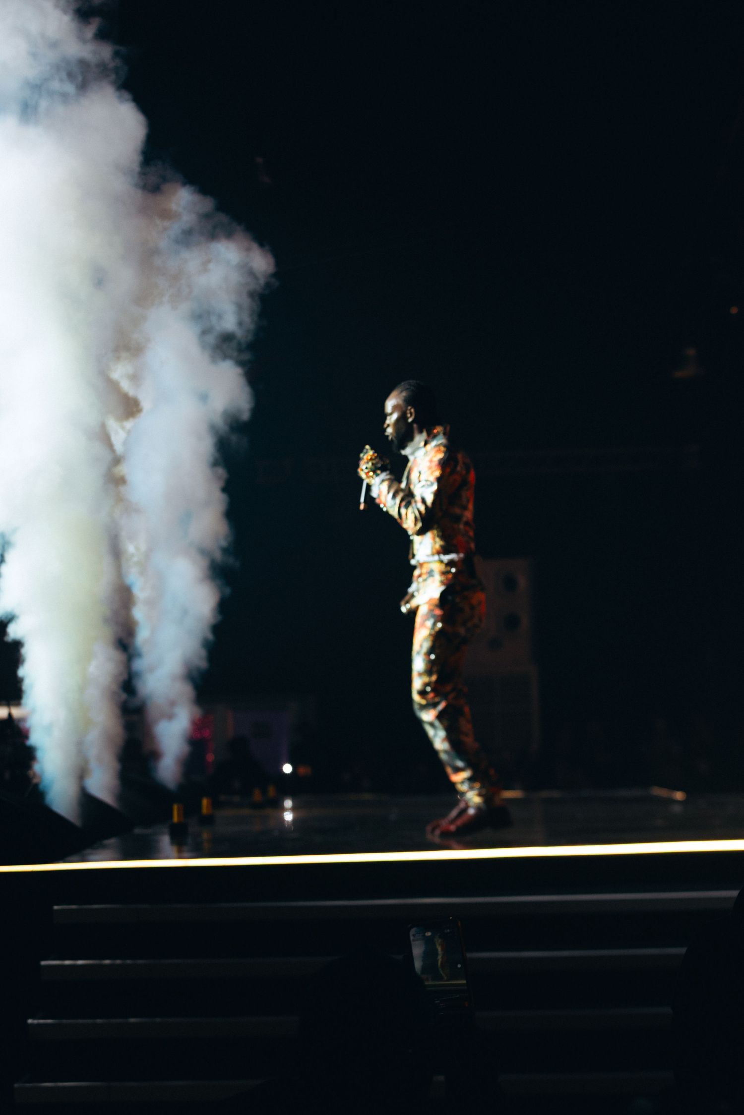 A performer sings on a dark stage surrounded by dramatic white smoke effects during a live concert.