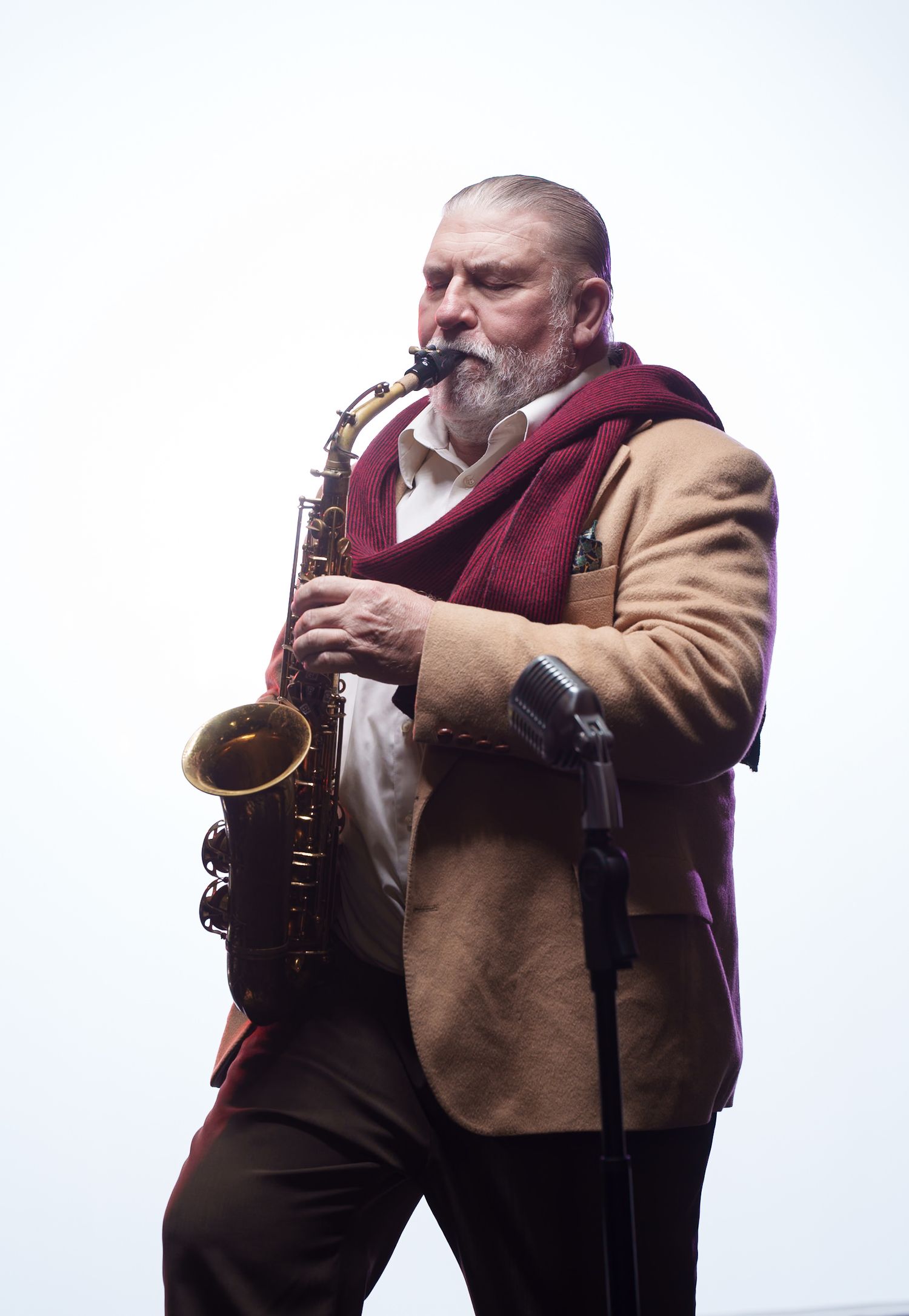 Saxophonist in burgundy scarf and tan jacket performing outdoors.