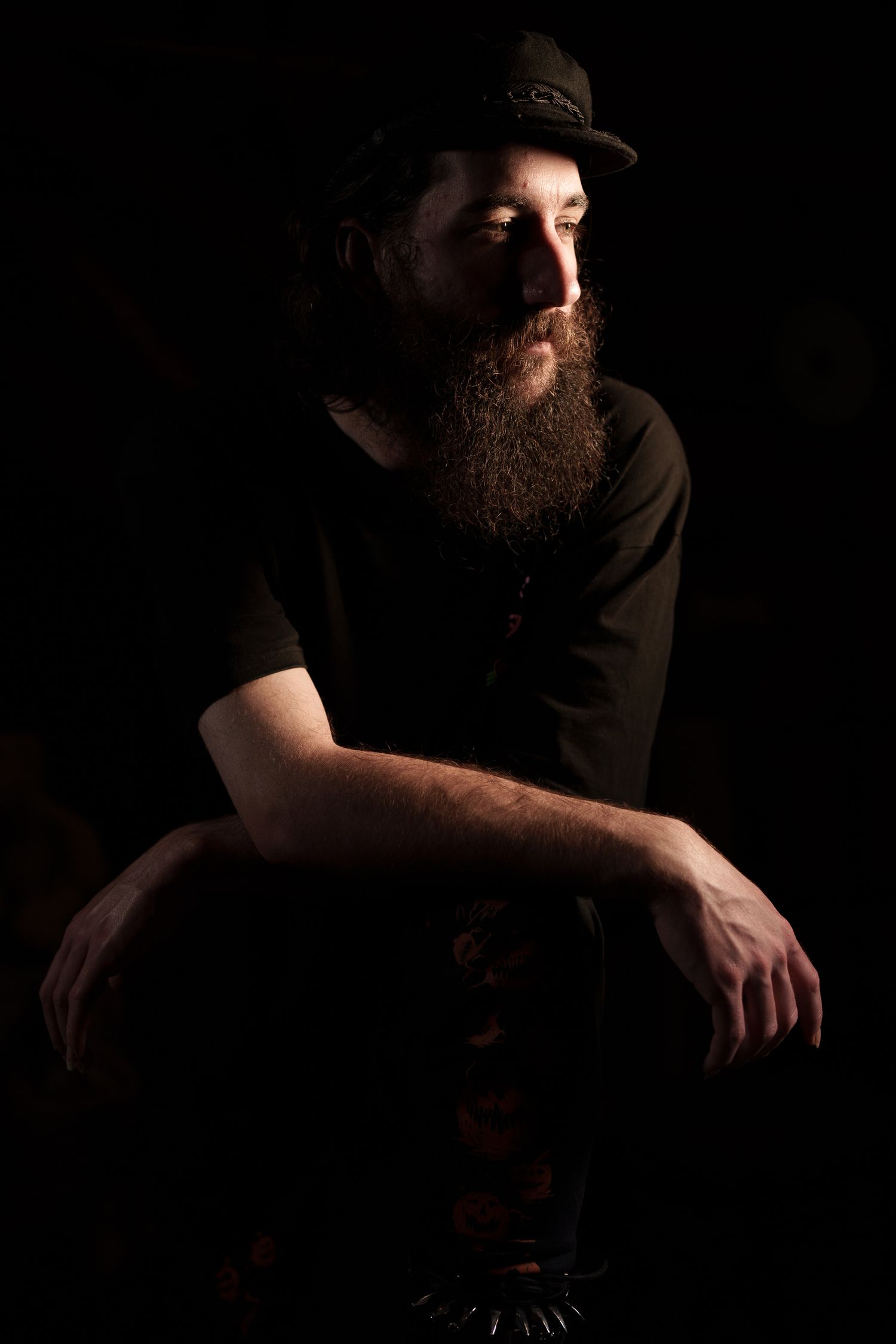 Low key portrait of bearded person in cap against dark background.