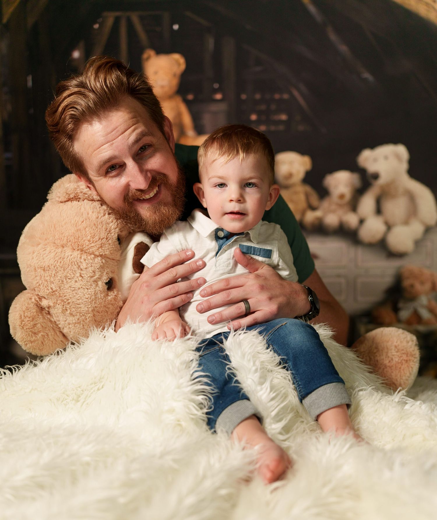 A cozy family portrait with stuffed teddy bears on a fluffy white rug in a rustic setting.