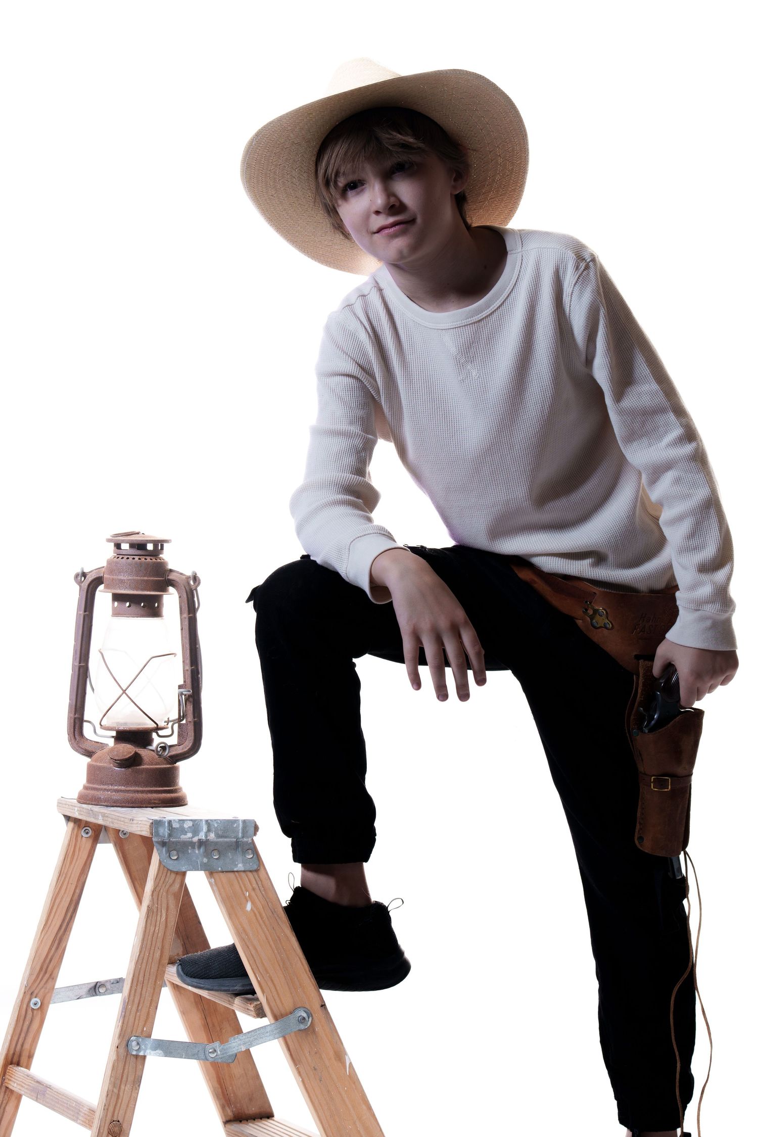 A stylish western look with beige hat, white sweater and dark pants, posed next to a vintage lantern on a ladder step.