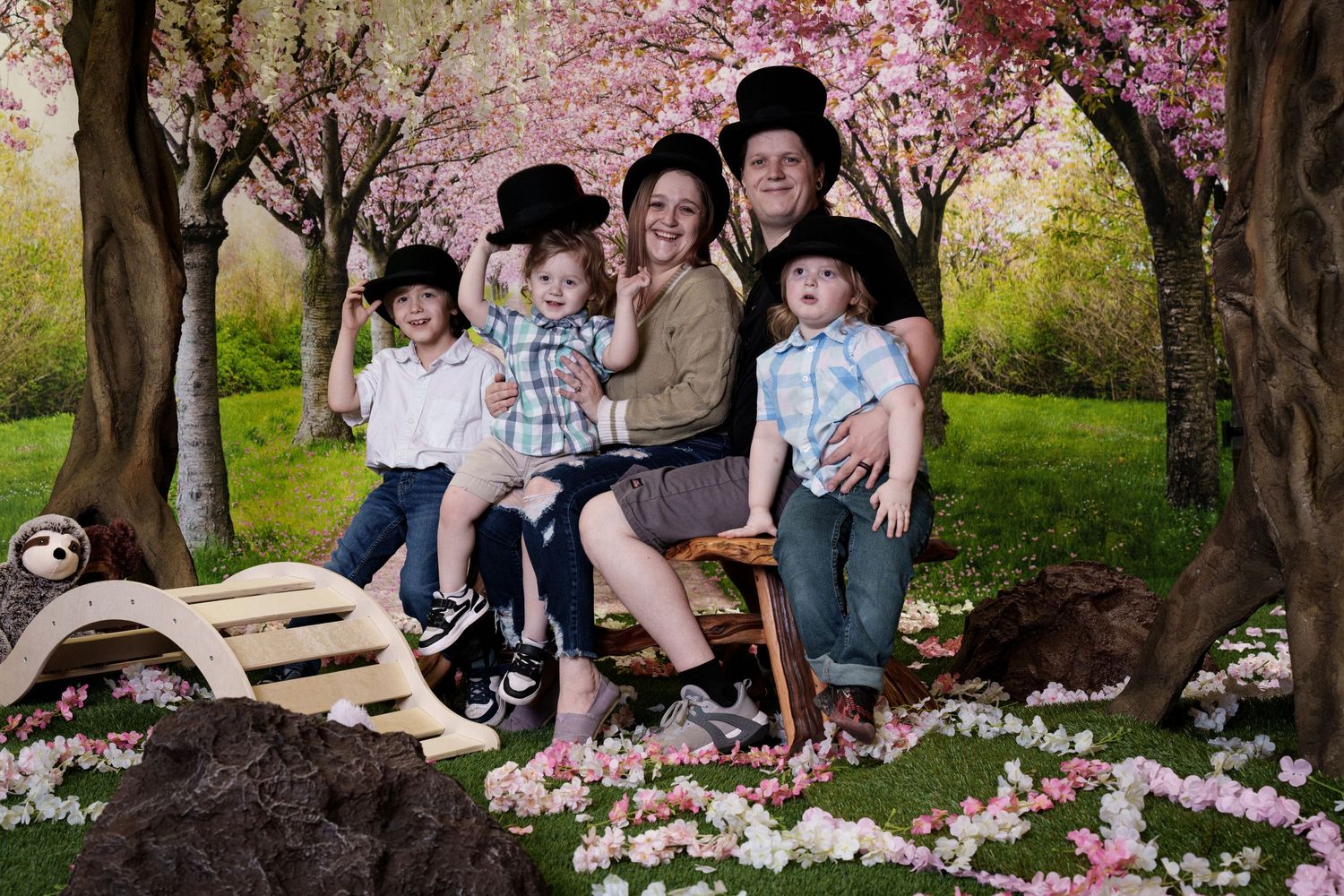 A springtime family portrait under blooming cherry blossom trees with pink petals scattered on the ground.