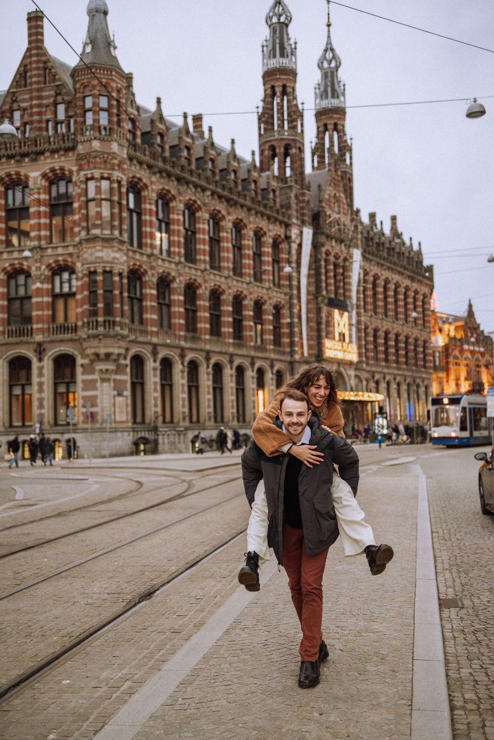 Playful couple having fun in front of historic European architecture with tram tracks.