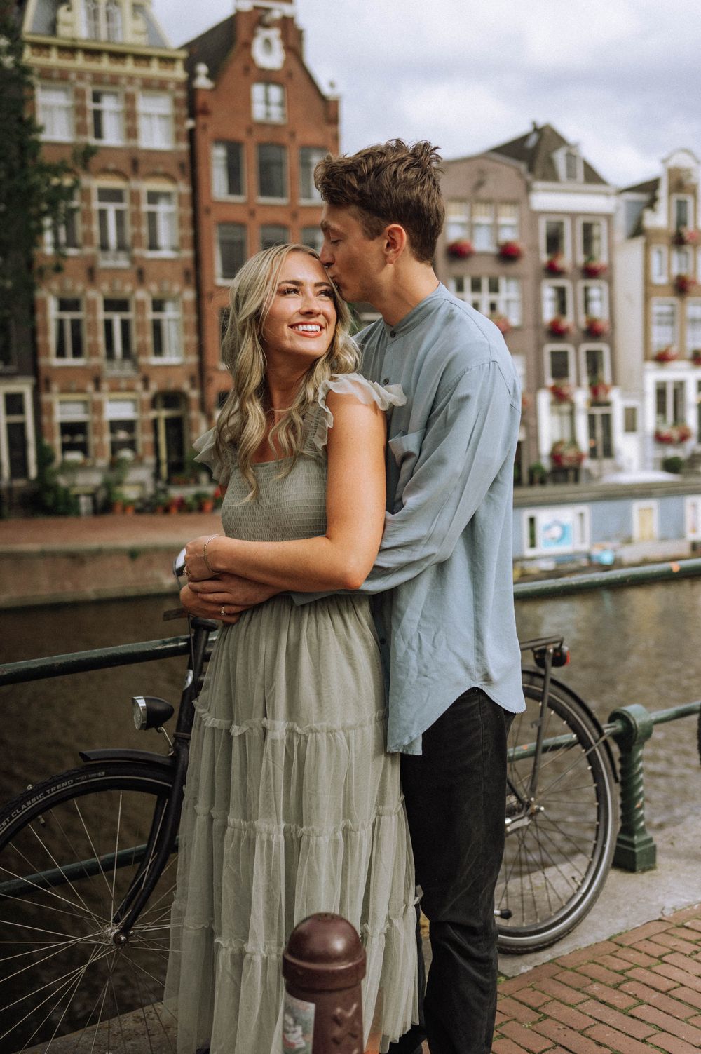 A couple shares a romantic moment along an Amsterdam canal with bicycles and historic buildings.